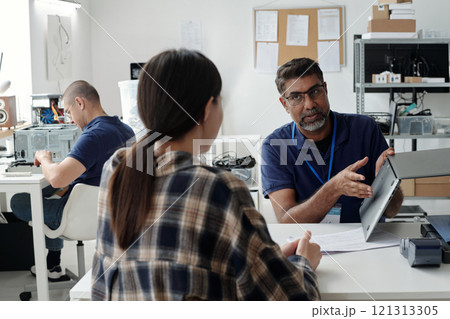 Meeting in progress with three professionals discussing technical details in modern office environment. Man holding tablet while explaining information to colleagues Meeting in progress with three professionals discussing technical details in modern office environment. Man holding tablet while explaining information to colleagues 121313305