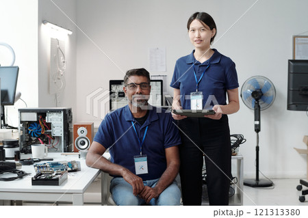 Two professionals working on electronic equipment in modern office setting, displaying camaraderie and teamwork with office equipment and components visible in background Two professionals working on electronic equipment in modern office setting, displaying camaraderie and teamwork with office equipment and components visible in background 121313380