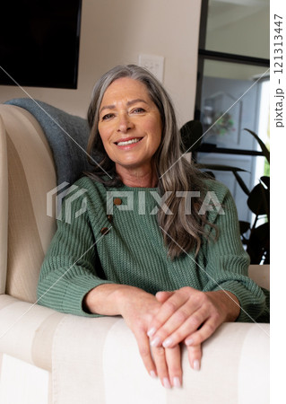 Smiling mature woman in green sweater relaxing at home, feeling content 121313447