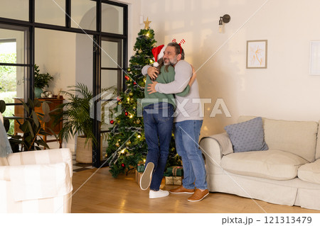 Mature couple hugging by Christmas tree at home, celebrating holiday together 121313479