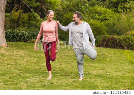 Mature couple enjoying outdoor exercise together, balancing on one leg in park 121313489