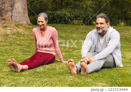 Mature couple stretching on grass, enjoying outdoor exercise and relaxation together 121313494