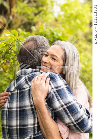 Mature couple embracing outdoors, woman smiling warmly in lush garden Mature couple embracing outdoors, woman smiling warmly in lush garden 121313531
