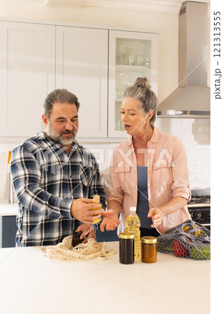 Mature couple organizing groceries in kitchen, sharing conversation and smiles, at home Mature couple organizing groceries in kitchen, sharing conversation and smiles, at home 121313555