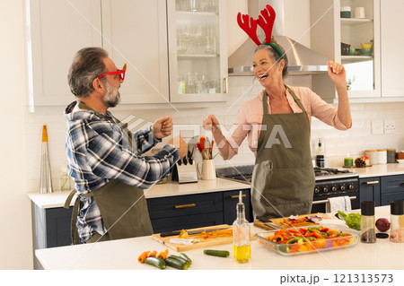 Christmas time, mature couple dancing joyfully in kitchen while preparing meal, at home Christmas time, mature couple dancing joyfully in kitchen while preparing meal, at home 121313573