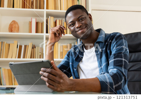 African American man using tablet at home, smiling and relaxing in library African American man using tablet at home, smiling and relaxing in library 121313751