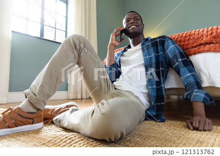 At home, African American man sitting on floor, talking on smartphone, smiling 121313762