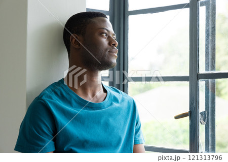 African American man gazing out window, reflecting peacefully at home 121313796