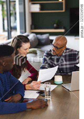 Diverse couple and biracial male financial advisor using laptop and discussing documents at home 121314546