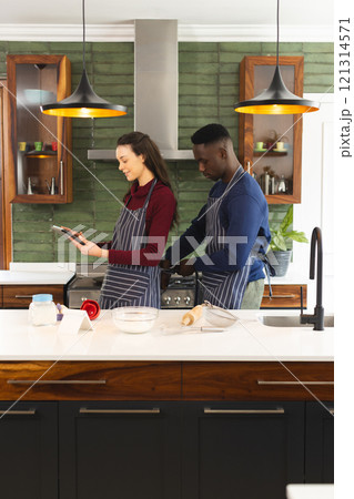 Happy diverse couple baking together in kitchen, using tablet at home 121314571