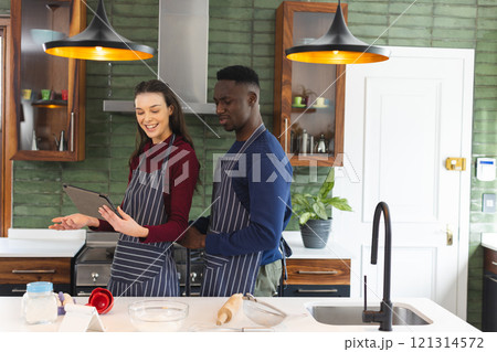Happy diverse couple baking together in kitchen, using tablet at home, copy space 121314572