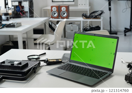 Showing a modern technology workspace featuring several gadgets including a laptop with a green screen. The background includes desks and various electronic devices providing a tech-savvy environment Showing a modern technology workspace featuring several gadgets including a laptop with a green screen. The background includes desks and various electronic devices providing a tech-savvy environment 121314760