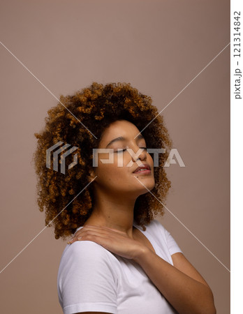 Biracial woman with dark curly hair, with hand on shoulder and closed eyes, copy space 121314842