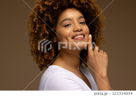 Happy biracial woman with dark curly hair touching face and smiling 121314854