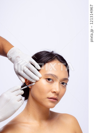 Hands of beautician in white surgical gloves injecting botox in cheek of asian woman, copy space 121314967
