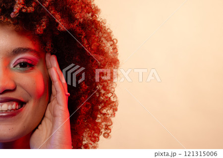 Smiling biracial woman with curly hair in pink eyeshadow and lipstick touching face, copy space Smiling biracial woman with curly hair in pink eyeshadow and lipstick touching face, copy space 121315006