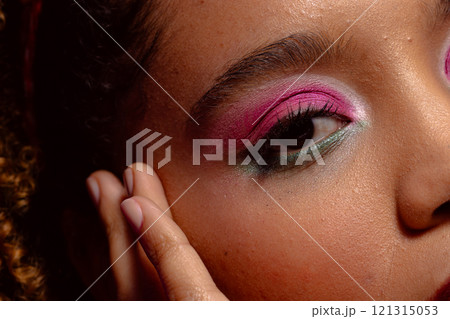 Close up of biracial woman with pink eye shadow and lipstick touching face, purple background Close up of biracial woman with pink eye shadow and lipstick touching face, purple background 121315053