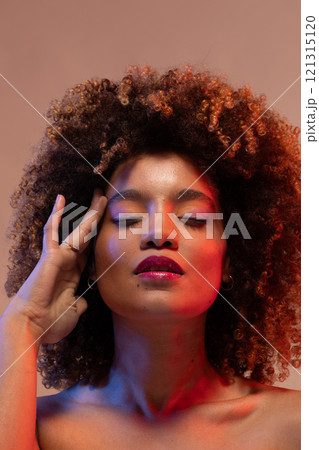 Biracial woman with curly hair and eyes closed touching temple in red light Biracial woman with curly hair and eyes closed touching temple in red light 121315120