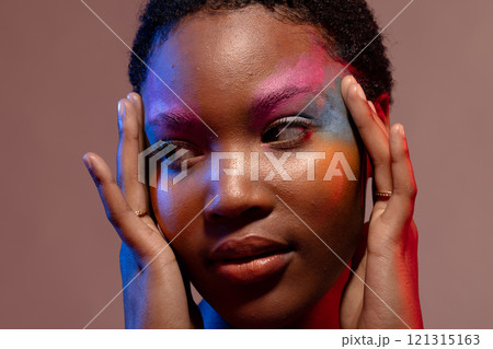 African american woman with short hair and colourful make up, looking away and touching temples 121315163