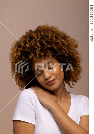 Smiling biracial woman with curly hair with hand on shoulder and closed eyes Smiling biracial woman with curly hair with hand on shoulder and closed eyes 121315261