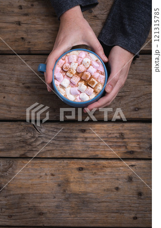 Hands of woman holding mug of hot chocolate drink with copy space at wooden table in cafe Hands of woman holding mug of hot chocolate drink with copy space at wooden table in cafe 121315785