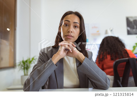 Thoughtful biracial businesswoman sitting at desk making video call in modern office 121315814