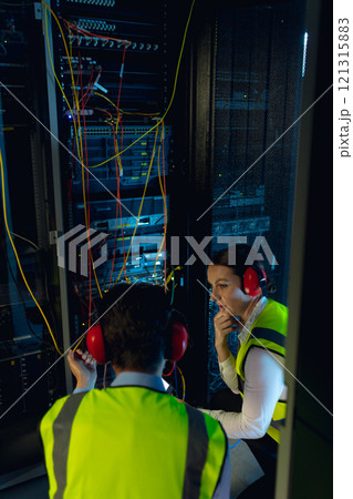 Diverse male and female engineers discussing together while inspecting iin computer server room Diverse male and female engineers discussing together while inspecting iin computer server room 121315883