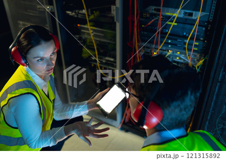 Diverse male and female engineer using digital tablet while inspecting in computer server room Diverse male and female engineer using digital tablet while inspecting in computer server room 121315892