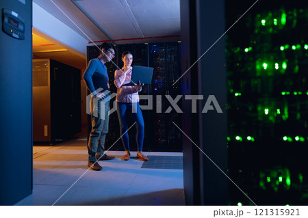 Diverse male and female engineers using laptop in computer server room 121315921