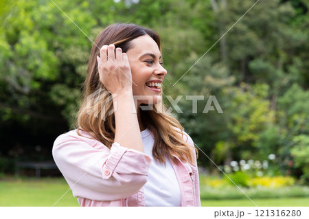 Smiling woman enjoying nature in park, feeling joyful and relaxed outdoors 121316280