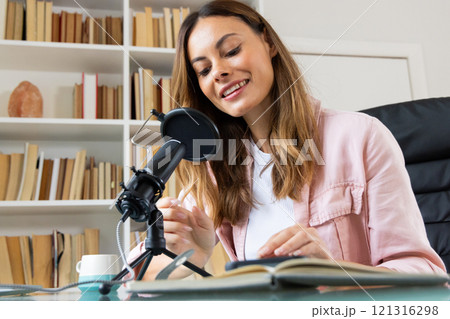 Smiling woman recording podcast at home with microphone and notebook 121316298