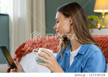 Relaxing at home, woman enjoying coffee while browsing tablet in cozy room 121316316