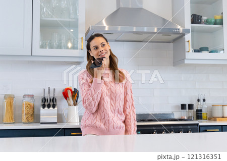 In kitchen, woman in pink sweater smiling and holding spatula, feeling joyful, at home 121316351