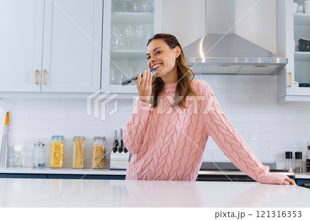 Smiling woman in kitchen singing into microphone, enjoying festive moment, at home 121316353