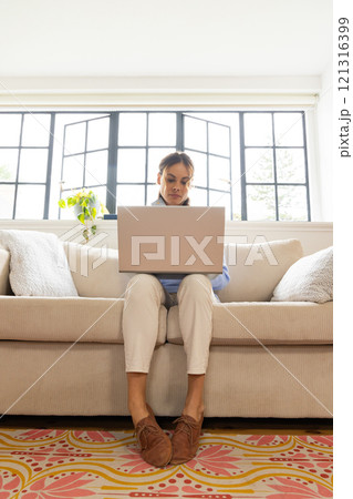 Woman using laptop on cozy sofa at home, focusing on work 121316399