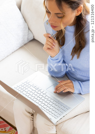 Woman shopping online using laptop and credit card at home, looking thoughtful Woman shopping online using laptop and credit card at home, looking thoughtful 121316400