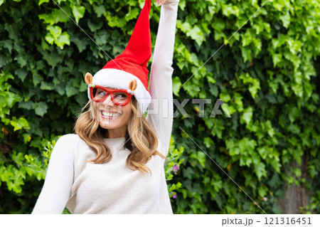 Christmas time, Smiling woman wearing Santa hat and festive glasses celebrating outdoors Christmas time, Smiling woman wearing Santa hat and festive glasses celebrating outdoors 121316451