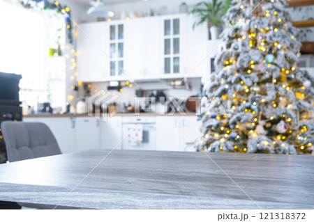 Grey Wooden empty table to demonstrate product with space for text with upholstered chairs in white kitchen, modern interior with Christmas tree and fairy lights. New Year, Christmas mood, cozy home. Grey Wooden empty table to demonstrate product with space for text with upholstered chairs in white kitchen, modern interior with Christmas tree and fairy lights. New Year, Christmas mood, cozy home. 121318372