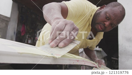 Front view of an African male panel beater in a township workshop, painting body of a car, slow moti 121319776