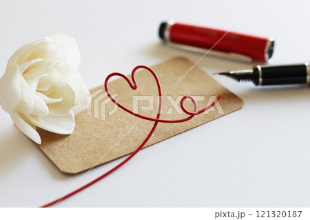 白いソラフラワーと茶色のメッセージカード　赤い万年筆で書くイメージ　赤いハートのワイヤー 121320187