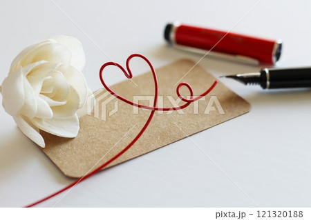白いソラフラワーと茶色のメッセージカード　赤い万年筆で書くイメージ　赤いハートのワイヤー 121320188