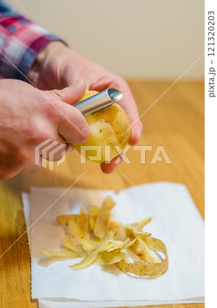 Close-up of a person peeling a potato with a vegetable peeler. High quality photo 121320203