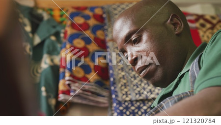 Side view low angle of an African male tailor in a township workshop, working with colourful fabrics 121320784