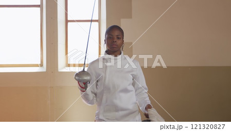 Portrait of a focused biracial female fencer athlete during a fencing training in a gym, walking wea 121320827