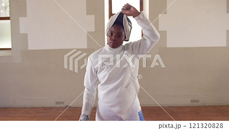Portrait of a happy biracial female fencer athlete during a fencing training in a gym, walking weari 121320828