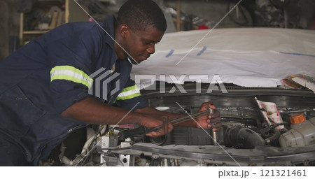 Side view of an African male car mechanic in a township workshop, repairing a car with a car boot op Side view of an African male car mechanic in a township workshop, repairing a car with a car boot op 121321461
