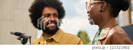 Smiling friends sharing a moment outdoors while enjoying food and conversation near a bicycle on a warm day 121321902