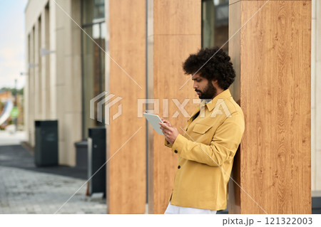 Office worker standing and concentrating while utilizing a tablet device against wooden pillars outside modern building Office worker standing and concentrating while utilizing a tablet device against wooden pillars outside modern building 121322003