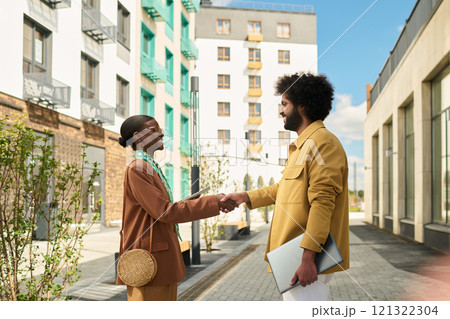 Two professionals exchanging handshake outdoors near modern apartment structures, initiating collaborative conversation in urban environment 121322304