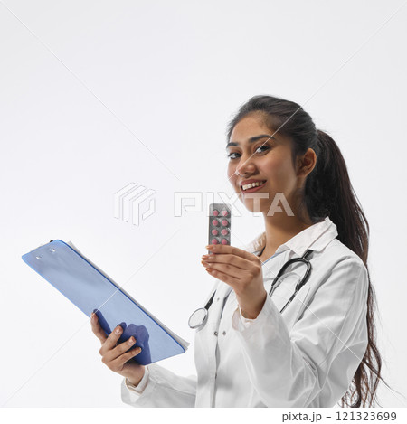 Portrait of charming Indian woman, dressed as therapist, posing with clipboard and shoeing blister of medicine treatments against white studio background. 121323699